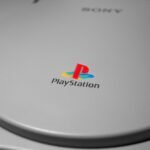 Detalhe do console PlayStation original em cinza, com o logotipo colorido da marca em destaque