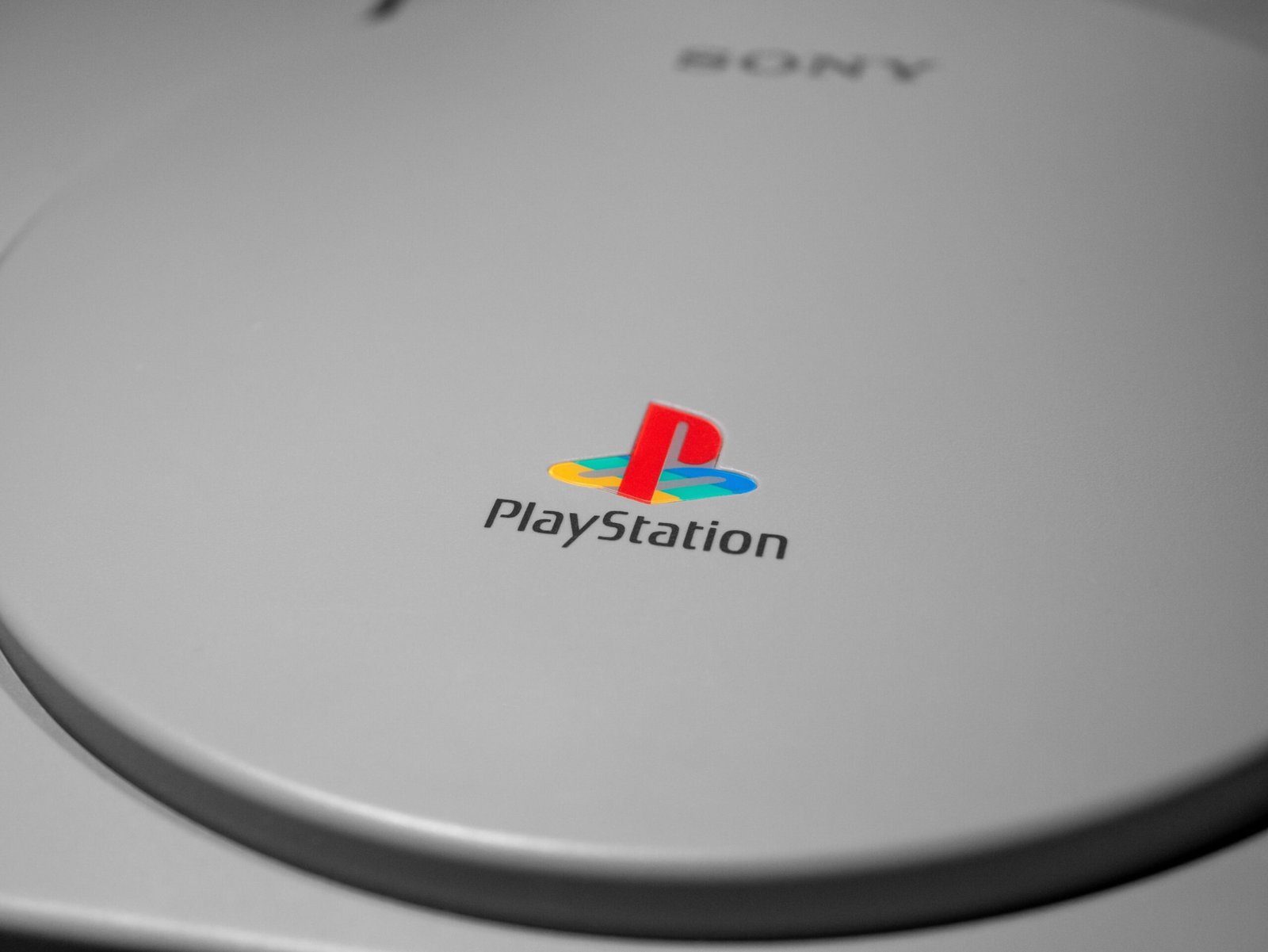 Detalhe do console PlayStation original em cinza, com o logotipo colorido da marca em destaque